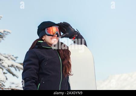 Foto di scorta di una ragazza che tiene il suo snowboard e occhiali su una montagna innevata Foto Stock