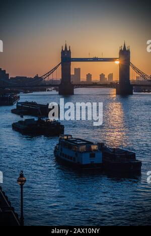 Alba dietro il Tower Bridge a Londra in una mattinata d'inverno con barche ormeggiate sul Tamigi Foto Stock