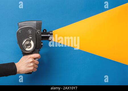 Mano femmina che tiene vecchio stile film fotocamera imitazione processo di ripresa su uno sfondo blu con luce gialla che arriva attraverso l'obiettivo Foto Stock