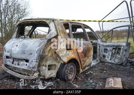Vista laterale vicino di isolato, bruciato fuori Renault Scenic auto abbandonato sulla terra desolata del Regno Unito. Vandalismo e criminalità automobilistica nel Regno Unito. Polizia consapevole. Foto Stock