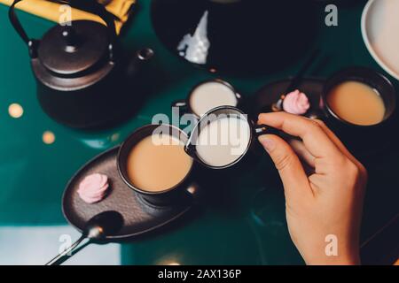 Donna che versa latte in tazza di tè dal bollitore Foto Stock