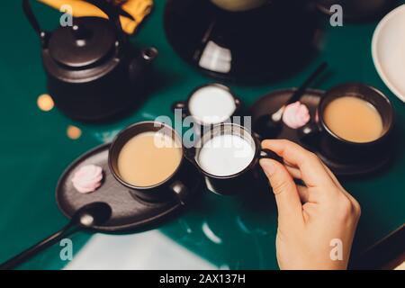 Donna che versa latte in tazza di tè dal bollitore Foto Stock