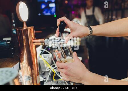 Close up di un barista maschio erogazione di birra in un pub tenendo un grande vetro il boccale sotto un rubinetto attacco su un acciaio inossidabile barile. Foto Stock