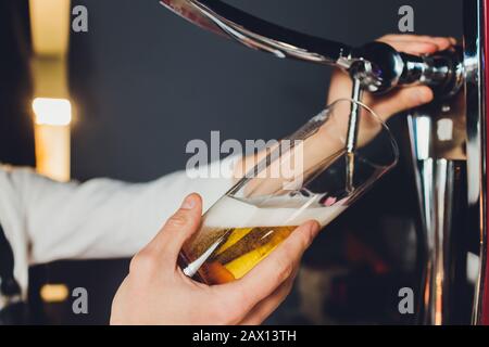 Close up di un barista maschio erogazione di birra in un pub tenendo un grande vetro il boccale sotto un rubinetto attacco su un acciaio inossidabile barile. Foto Stock