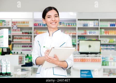 primo piano farmacista con sorriso sul viso che fa note in negozio di droga Foto Stock