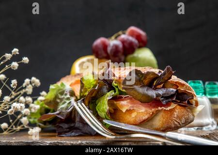 Un delizioso panino di pane al sesamo affumicato su un piatto di legno. È perfetto da mangiare con insalate e formaggi saporiti. Cibo sano per la colazione. Foto Stock