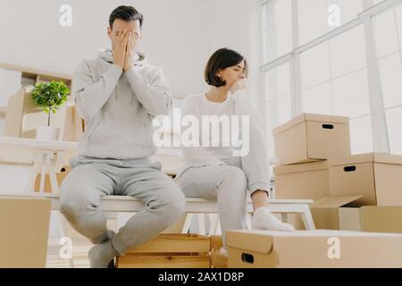 La coppia preoccupata posa vicino pila di scatole di cartone, devono muoversi in altro appartamento, non hanno soldi per affitto, hanno rifiutato espressioni tristi, sedersi insieme dentro Foto Stock