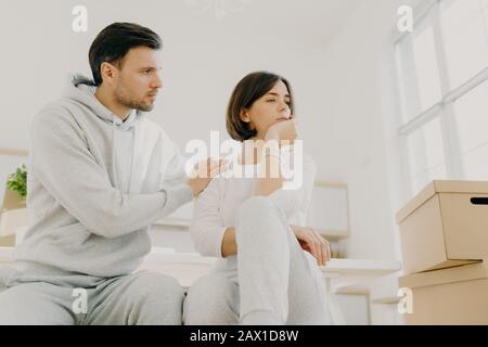Il marito attento cerca di calmare la moglie in una situazione di vita difficile, trasferirsi in una nuova casa per vivere, posare al chiuso vicino scatole di cartone, risolvere il problema domestico Foto Stock