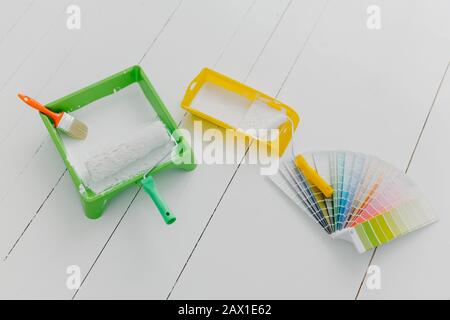 Vista dall'alto di vassoi di verniciatura, pennelli e rulli, campione di tavolozza dei colori, pavimento bianco. Attrezzi per fare riparare e rimodellamento della casa. Concetto di design Foto Stock