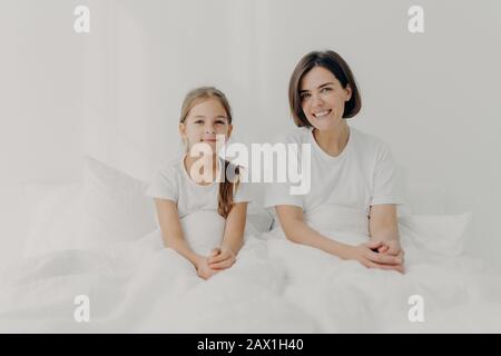 Al coperto di mamma felice e piccola figlia si sentono rilassato e felice posa a letto, godere di comfort, trascorrere il tempo libero a casa, svegliarsi tardi, hanno abbastanza Foto Stock