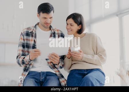 Un bicchierino interno di documenti di studio di felice moglie e marito ricevuti dalla banca, fare insieme la documentazione, bere caffè aromatico, stare a stretto contatto l'uno con l'altro, Foto Stock