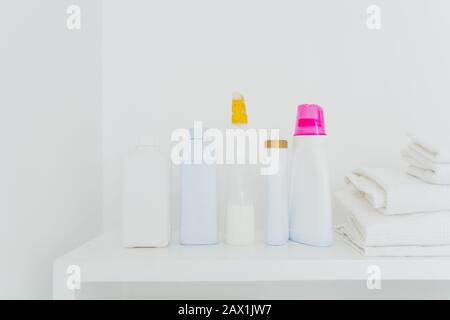 Pila di asciugamani bianchi piegati e bottiglie con detergente su fondo bianco. Concetto di pulizia e lavaggio. Spazio per il testo Foto Stock