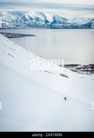 Un uomo che scia in discesa con oceano e montagne sullo sfondo Foto Stock