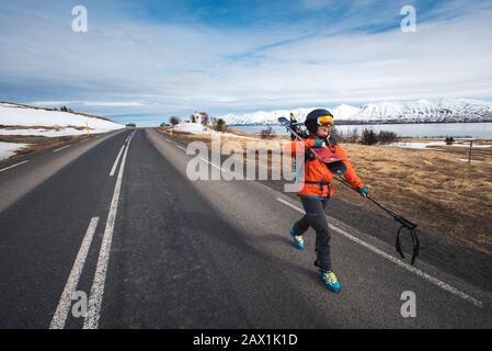 Una donna che cammina lungo una strada asfaltata con sci in Islanda Foto Stock