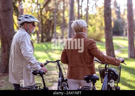 Donna anziana e uomo in parco con biciclette Foto Stock