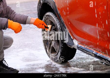 Pulizia con sapone in caso di autolavaggio self-service. Uomo in gomma  guanti lava ruota nera della sua auto arancione con spazzola. L'acqua  saponata si esaurisce Foto stock - Alamy