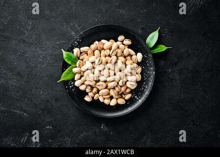 Pistacchi di sale in una ciotola su uno sfondo nero. Vista dall'alto. Spazio libero per il testo. Foto Stock