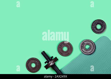Foto sportiva. Dumbbells situato su tappeto sportivo su sfondo verde menta. Disposizione piatta, vista dall'alto, spazio di copia. Foto Stock