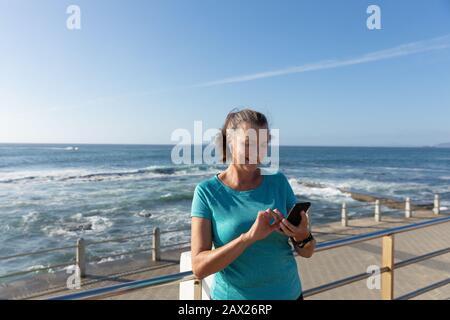 Jogger femmina utilizzando il telefono cellulare sul mare Foto Stock