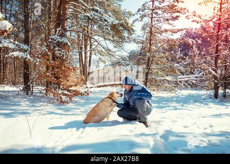 L'uomo e il cane sono i migliori amici. L'uomo e il cane sono seduti in una foresta nevosa in una giornata di sole invernale Foto Stock