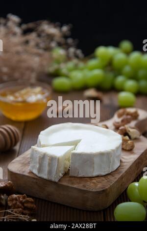 Formaggi di capra su sfondo ligneo con miele e uva. Foto di cibo scuro. Foto Stock