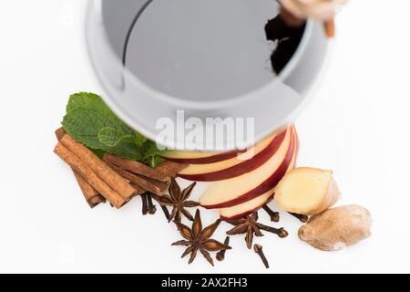 Concetto di degustazione di vini nazionali. Bastoncini di cannella, foglie di menta, anice, zenzero, fette di mela e garofano in vetro. Bicchiere di vino rosso su sfondo bianco. Cabernet o merlot in vetro con spezie. Foto Stock