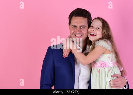 Ragazza e uomo con facce sorridenti felici su sfondo rosa. Figlia e padre si abbracciano, copiare spazio. La scolaretta si trova accanto al suo padre. Concetto di infanzia e famiglia. Foto Stock