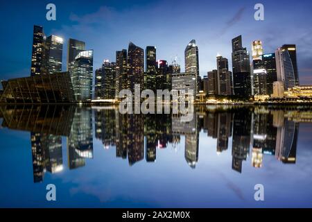 Lo skyline cittadino di Singapore di notte mostra gli edifici degli uffici nel quartiere finanziario che si riflette sull'acqua. Foto Stock