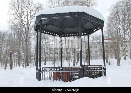 Gazebo in metallo aperto con panchine nel parco, coperto di neve in giornate nuvolose. Concetto di miglioramento e decorazione dell'ambiente urbano. Foto di scorta per Web, stampa, sfondo e sfondo. Foto Stock