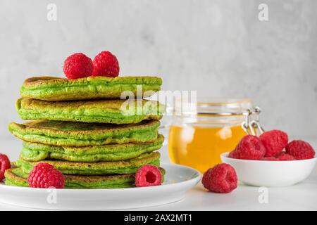 Frittelle verdi con tè matcha, lamponi e miele. Colazione sana, dessert. Primo piano Foto Stock