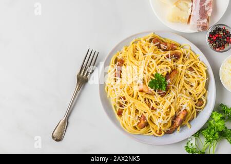Pasta classica italiana fatta in casa carbonara con pancetta, uova, parmigiano e prezzemolo in un piatto con forchetta su tavolo in marmo bianco. Vista dall'alto con copia Foto Stock