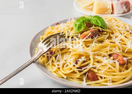 Pasta italiana carbonara a base di spaghetti, pancetta, parmigiano e basilico in un piatto con forchetta su tavolo in marmo bianco. Primo piano Foto Stock