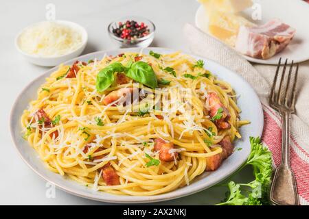 Pasta classica italiana fatta in casa carbonara con pancetta, uova, parmigiano e prezzemolo in un piatto con forchetta su tavolo di marmo bianco. Primo piano Foto Stock