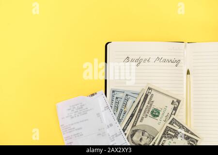 Spese e pianificazione di bilancio. Sopra la vista delle banconote in dollari, penna, fatture e taccuino su sfondo giallo con spazio di copia. Vista dall'alto, piatto Foto Stock