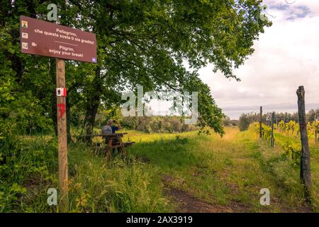 Segno del pellegrino sulla via francigena con la donna pellegrina che riposa su un tavolo in legno con lo zaino rivolto verso il Lago di Bolsena Italia Foto Stock