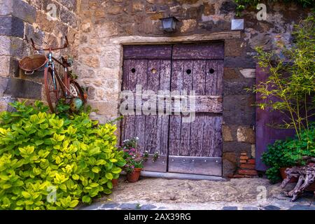 Bella posizione a Bolsena molto vecchia bici arrugginita appesa Muro accanto ad un'antica porta boscosa Italia Foto Stock