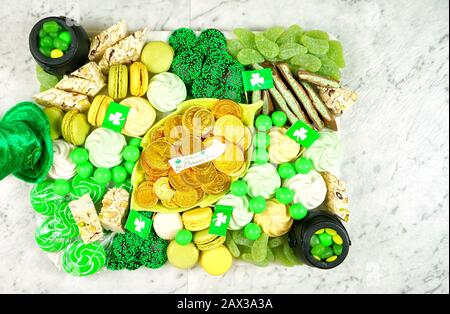 Happy St Patrick's Day salumi dessert piatto di pascolo con monete d'oro al cioccolato, caramelle, biscotti, pentole d'oro e cappelli leprechaun su tavolo di marmo Foto Stock