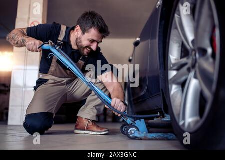 Meccanico automatico professionale che sostituisce uno pneumatico in officina di riparazione auto.ruota di auto di cambio uomo in officina di riparazione auto. Foto Stock