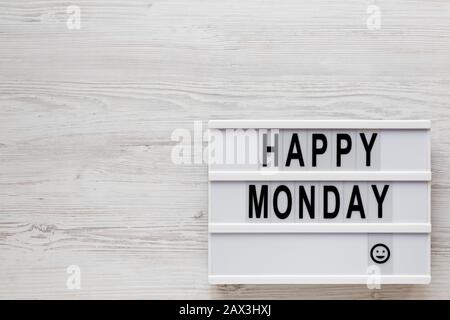 Parole 'happy monday' su un lightbox, appunti con foglio di carta vuoto su uno sfondo di legno bianco, vista dall'alto. Sopra, dall'alto, disposizione piana. Copia Foto Stock