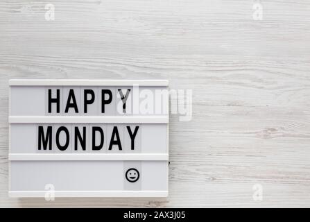 Parole 'happy monday' su una tavola moderna, appunti con foglio di carta bianco su una superficie di legno bianco, vista dall'alto. Sopra, dall'alto, disposizione piana. Spazio Foto Stock