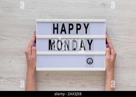 Le mani femminili tengono un lightbox con parole 'happy monday' su sfondo bianco di legno, vista dall'alto. Sopra, dall'alto, disposizione piana. Primo piano. Foto Stock