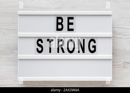 Parole 'essere forti' su una scatola luminosa su una superficie di legno bianco, vista dall'alto. Sopra, dall'alto, disposizione piana. Foto Stock
