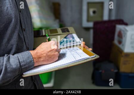 Ispettore che tiene un notebook in mano durante un'ispezione a casa nel seminterrato, primo piano e fuoco selettivo di un uomo che prende appunti professionali. Foto Stock