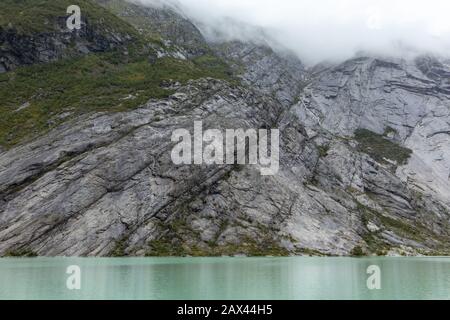 Norvegia montagne paesaggio vista lago con azzurro acqua, rocce, ghiacciaio, neve. Gita di monitoraggio di un giorno nuvoloso a Nigardsbreen a Jostedalsbreen nati Foto Stock