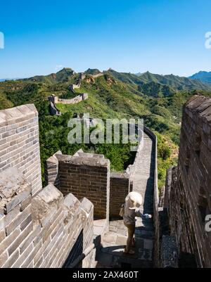 Donna che indossa cappello a testa larga dinastia Ming Jinshanling Grande Muraglia cinese con torri di guardia che conducono a distanza sulla cresta di montagna, Cina, Asia Foto Stock