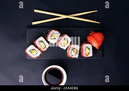 Rotoli su un supporto di granito per sushi sono disposti sotto forma di un drago, accanto a bastoni stand per sushi e salsa di soia. Foto Stock