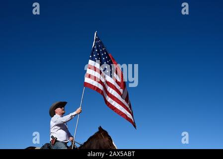 Un membro di un gruppo chiamato Cowboys per Trump, a cavallo, armato di una pistola e che porta una bandiera americana, partecipa a un rally pro-Trump. Foto Stock