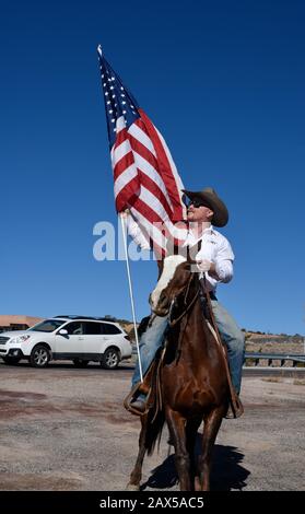 Un membro di un gruppo chiamato Cowboys per Trump, a cavallo, armato di una pistola e che porta una bandiera americana, partecipa a un rally pro-Trump. Foto Stock