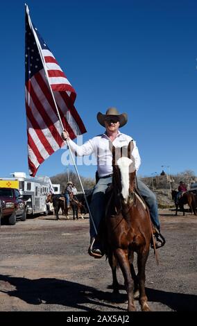 Un membro di un gruppo chiamato Cowboys per Trump, a cavallo, armato di una pistola e che porta una bandiera americana, partecipa a un rally pro-Trump. Foto Stock