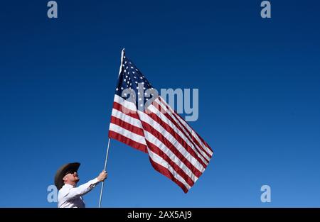 Un membro di un gruppo chiamato Cowboys per Trump, a cavallo, armato di una pistola e che porta una bandiera americana, partecipa a un rally pro-Trump. Foto Stock